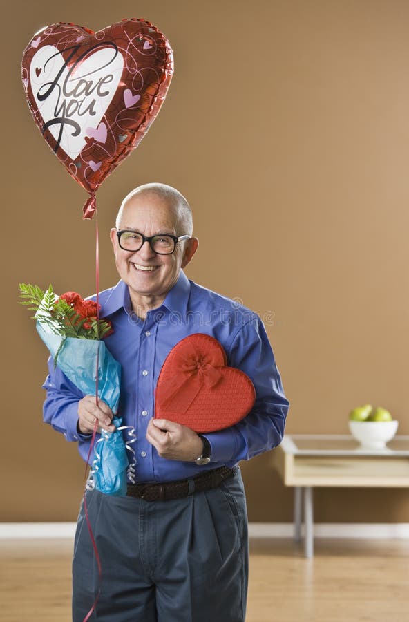 An elderly man is holding valentines gifts. He is smiling at the camera. Vertically framed shot. An elderly man is holding valentines gifts. He is smiling at the camera. Vertically framed shot.