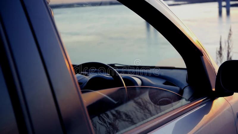 Человек раскрывает окно в автомобиле и восхищает красивый заход солнца на реке на мосте, сидя в автостоянке