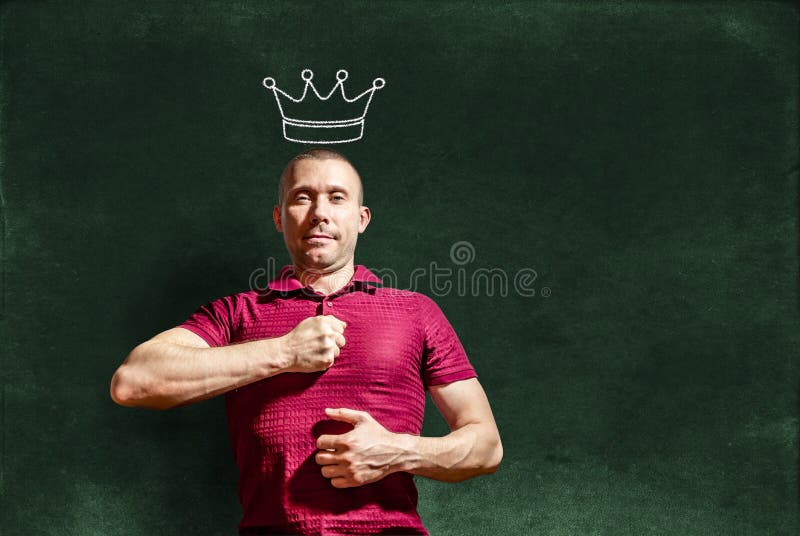 A smug man with a crown on his head hits his chest with his fist against the background of a chalkboard. A smug man with a crown on his head hits his chest with his fist against the background of a chalkboard