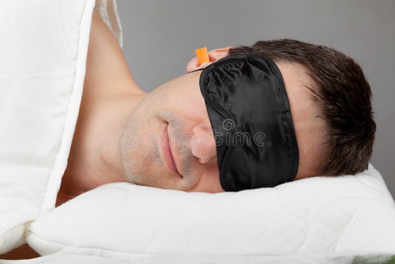 Человек с маской спать и earplugs в кровати стоковая фотография Человек с маской спать и earplugs в кровати стоковая фотография