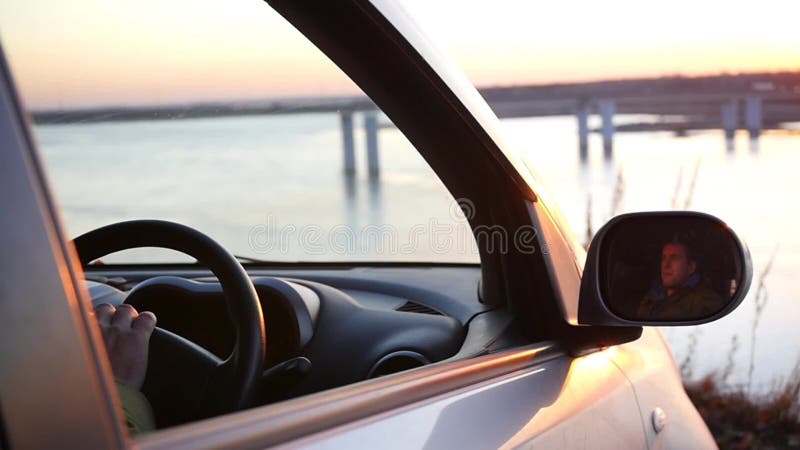 Человек сидит в автомобиле в месте для стоянки и восхищает красивый вид и заход солнца в открытом окне автомобиля