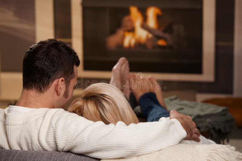 Couple sitting on sofa at home in front of fireplace, rear view. Couple sitting on sofa at home in front of fireplace, rear view.