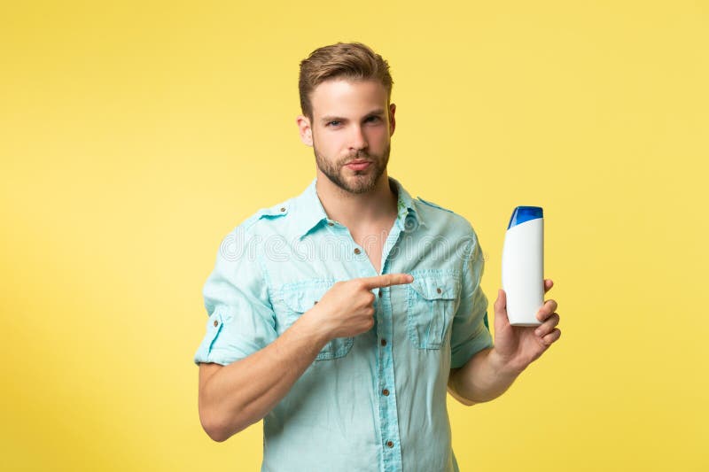 человек, указывающий пальцем на косметику после бритья. мужчина держит крем после бритья, изолированный на желтом.