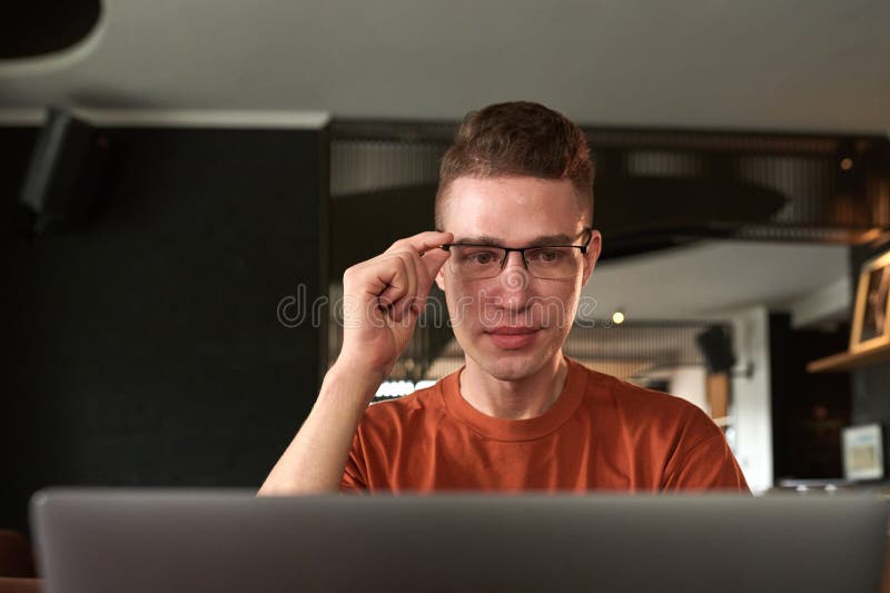 Smiling young man adjusting glasses when reading e-mails on laptop or looking for bugs. Smiling young man adjusting glasses when reading e-mails on laptop or looking for bugs