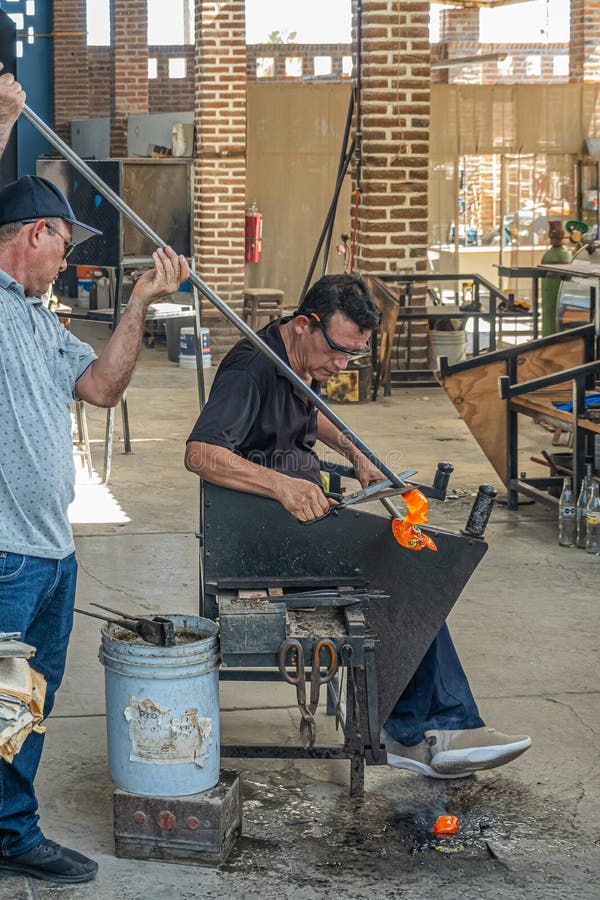 Mexico, Cabo San Lucas - July 16, 2023: La Fabrica de Vidrio Soplado. Hand blown artistic glass factory. 2 Men team work, glassblower handles shear and blowpipe, while other handles hot glass. Mexico, Cabo San Lucas - July 16, 2023: La Fabrica de Vidrio Soplado. Hand blown artistic glass factory. 2 Men team work, glassblower handles shear and blowpipe, while other handles hot glass