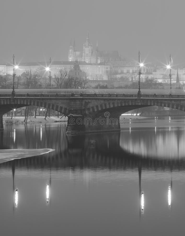 Черно-белое фото зимы моста через реку Влтавы отражая на поверхности воды и замке Праги стоковое фото rf Черно-белое фото зимы моста через реку Влтавы отражая на поверхности воды и замке Праги стоковое фото rf