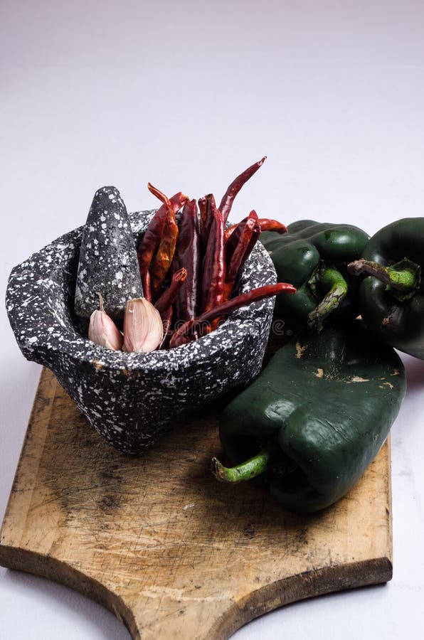 Черный каменный миномет с ингридиентами для соуса, перцами красного chili, сырцовыми гвоздичными деревьями чеснока стоковая фотография Черный каменный миномет с ингридиентами для соуса, перцами красного chili, сырцовыми гвоздичными деревьями чеснока стоковая фотография