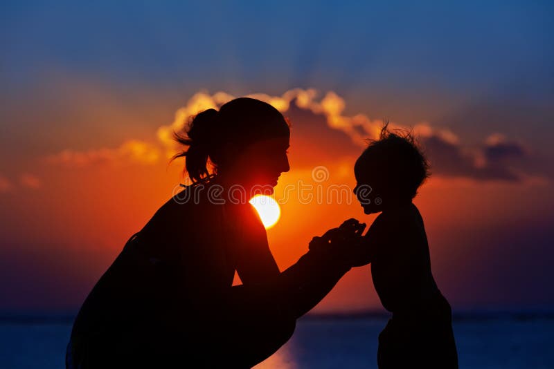 Happy family black silhouette on sunset sky background. Young mother, baby son have fun together, walk by sea beach. Barefoot child look at sun. Travel lifestyle, parents with kids on summer vacation. Happy family black silhouette on sunset sky background. Young mother, baby son have fun together, walk by sea beach. Barefoot child look at sun. Travel lifestyle, parents with kids on summer vacation