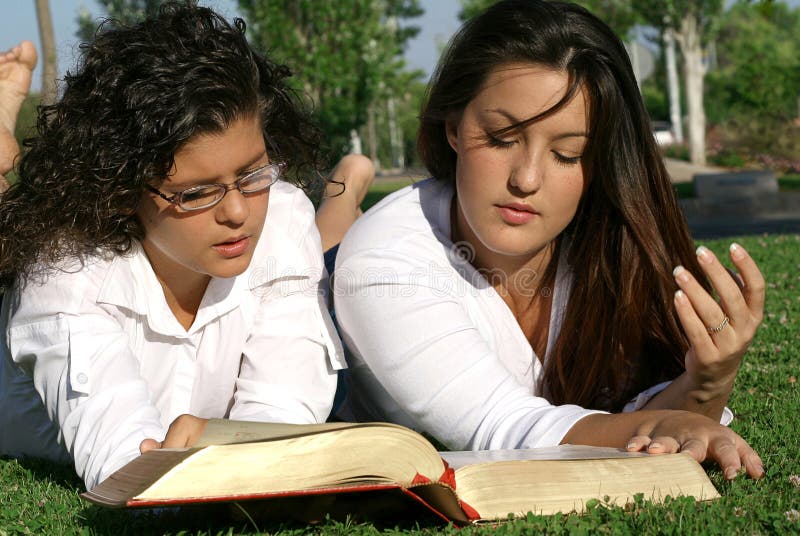 2 young women laying on grass reading bible. 2 young women laying on grass reading bible