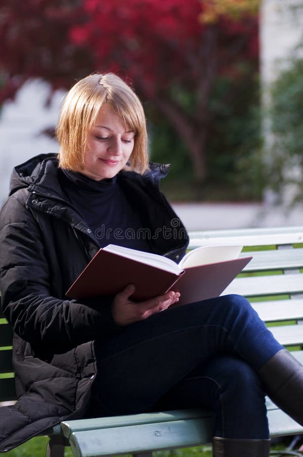 Girl reading a book on a park bench outside. Girl reading a book on a park bench outside