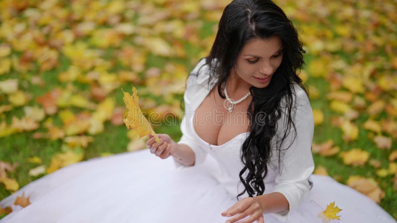 чувствительная невеста в день свадьбы осенью, но белая женщина в белом платье сидит на траве в парке сток-видео