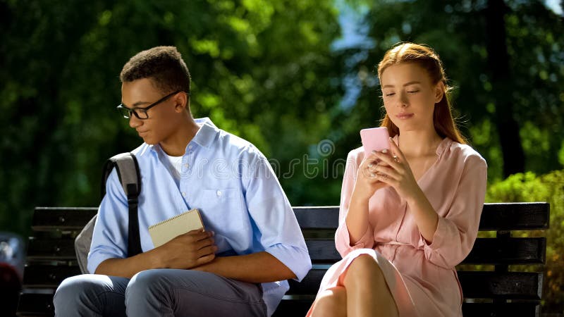 Shy geek sitting on bench with beautiful girl using smartphone, hesitation, stock photo. Shy geek sitting on bench with beautiful girl using smartphone, hesitation, stock photo