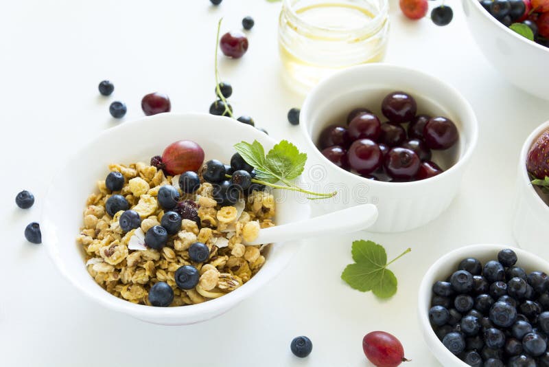 Шар домодельного granola с клубникой, голубикой, вишней, крыжовником, черной смородиной и медом на белой деревянной предпосылке стоковая фотография rf Шар домодельного granola с клубникой, голубикой, вишней, крыжовником, черной смородиной и медом на белой деревянной предпосылке стоковая фотография rf