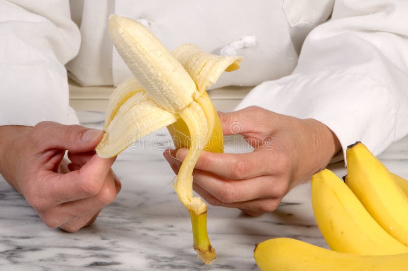 Strong close up action photograph of a uniformed Chef peeling a fresh banana atop a marble pastry slab. Strong close up action photograph of a uniformed Chef peeling a fresh banana atop a marble pastry slab.