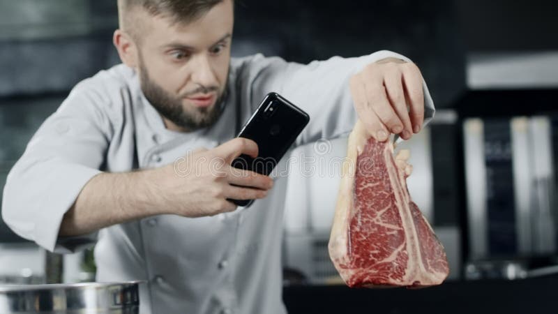 Шеф-повар делая фото мяса с мобильным телефоном Мужской шеф-повар принимая фото стейка