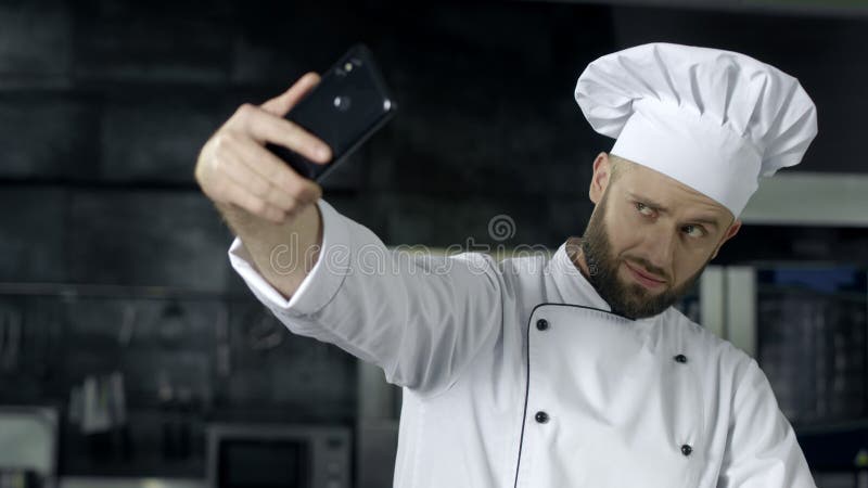 Шеф-повар делая фото на кухне Портрет шеф-повара принимая selfie на мобильный телефон