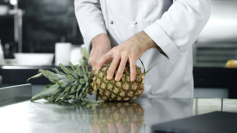 Шеф-повар прерывая ананас в замедленном движении Шеф-повар человека режа свежие фрукты