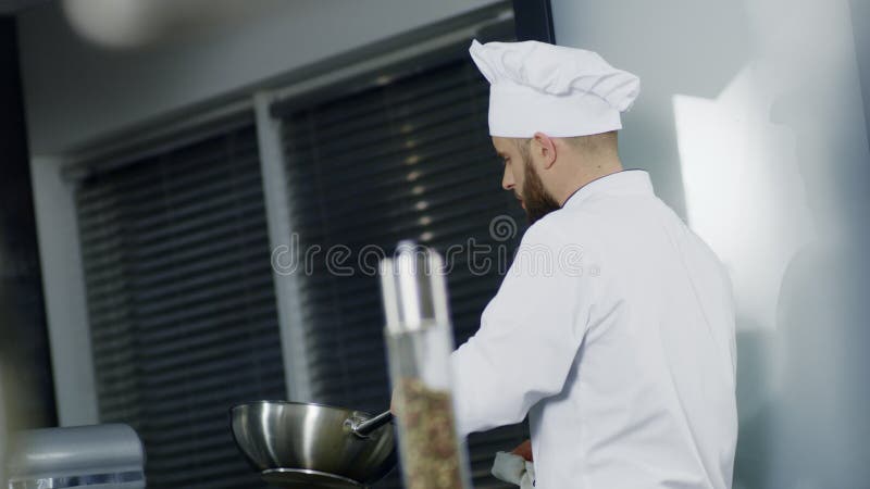 Шеф-повар человека варя во вке на кухне Сфокусированный шеф-повар подготавливая азиатскую еду