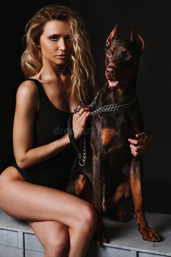 Шикарная белокурая женщина в черном bodysuit при Doberman смотря камеру Красивая девушка с длинными загоренными ногами стоковое фото Шикарная белокурая женщина в черном bodysuit при Doberman смотря камеру Красивая девушка с длинными загоренными ногами стоковое фото