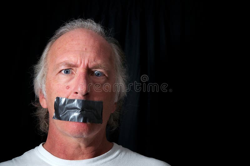Studio portrait of an older blue eyed man with mouth duct taped closed, looking distraught, black background with copy space. Political correctness or freedom of speech concept. Studio portrait of an older blue eyed man with mouth duct taped closed, looking distraught, black background with copy space. Political correctness or freedom of speech concept.