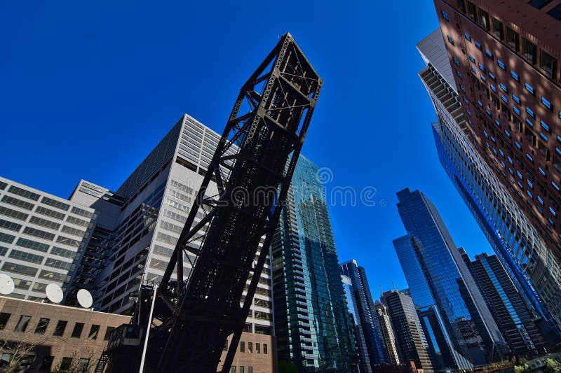 The downtown cityscape of skyscrapers and high rise buildings in Chicago Illiniois as viewed from the Chicago River in April 2023. An old steel lift bridge in the upright position over the river. The downtown cityscape of skyscrapers and high rise buildings in Chicago Illiniois as viewed from the Chicago River in April 2023. An old steel lift bridge in the upright position over the river