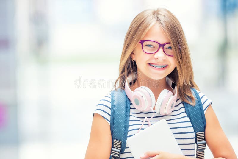 Schoolgirl with bag, backpack. Portrait of modern happy teen school girl with bag backpack headphones and tablet. Girl with dental braces and glasses. Schoolgirl with bag, backpack. Portrait of modern happy teen school girl with bag backpack headphones and tablet. Girl with dental braces and glasses.