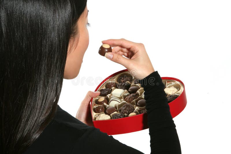A woman eating a piece of chocolate out of a heart shaped Valentines box. A woman eating a piece of chocolate out of a heart shaped Valentines box