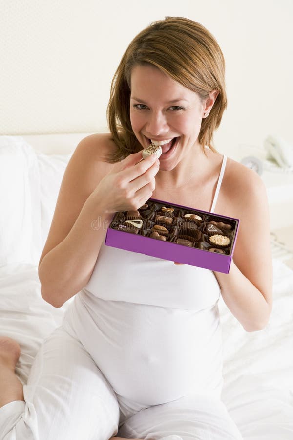 Pregnant woman in bed eating chocolate smiling at camera. Pregnant woman in bed eating chocolate smiling at camera