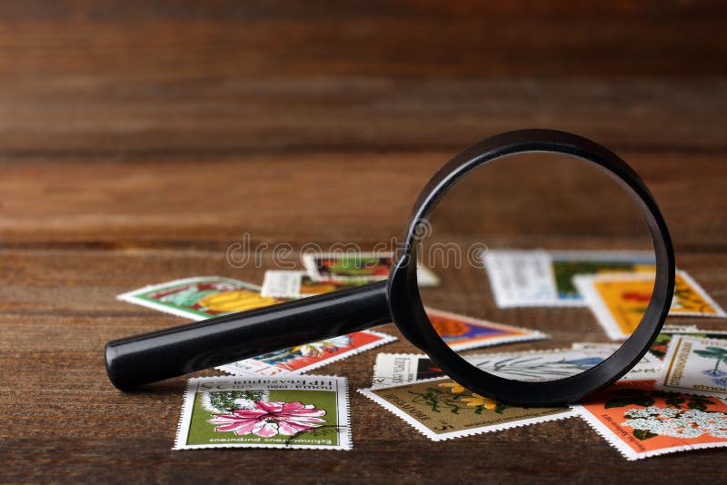 A small pile of expensive and collectible stamps with a magnifying glass on wooden brown table. A small pile of expensive and collectible stamps with a magnifying glass on wooden brown table