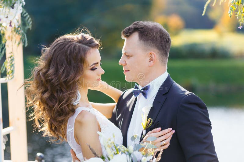 Элегантная курчавая невеста и счастливый groom outdoors на предпосылке озеро стоковая фотография rf Элегантная курчавая невеста и счастливый groom outdoors на предпосылке озеро стоковая фотография rf
