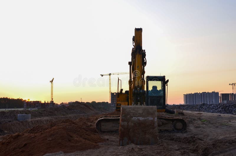 Экскаватор на строительной площадке на фоне заката. Earthmoving тяжелое оборудование для учреждения и trenchs земли digg стоковая фотография rf