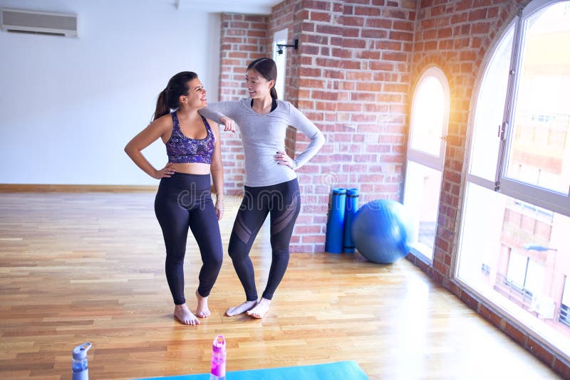 2 young beautiful sportswomen smiling happy. Standing speaking with smile on face after class of yoga at gym. 2 young beautiful sportswomen smiling happy. Standing speaking with smile on face after class of yoga at gym