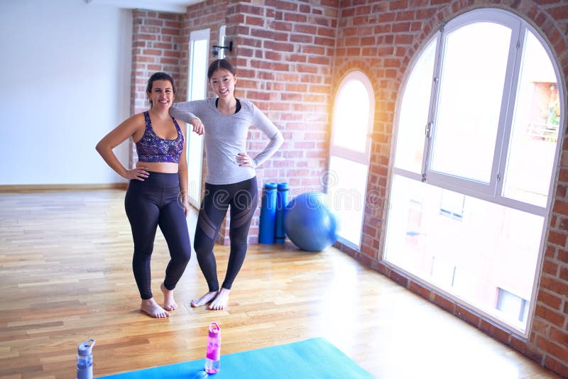 2 young beautiful sportswomen smiling happy. Standing speaking with smile on face after class of yoga at gym. 2 young beautiful sportswomen smiling happy. Standing speaking with smile on face after class of yoga at gym