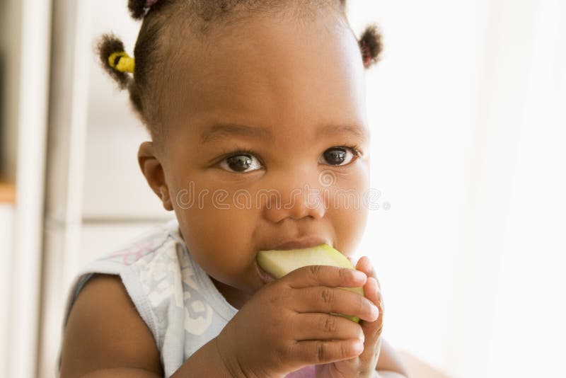Young girl eating apple indoors looking off camera. Young girl eating apple indoors looking off camera
