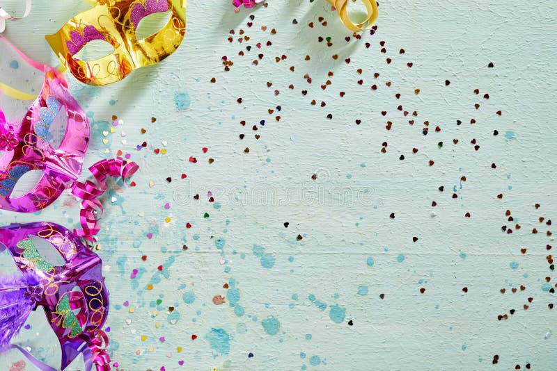 Brightly colored carnival or Mardi Gras border with metallic foil eye masks decorated with feathers and twirled streamers on a light blue wood background with scattered confetti and copy space. Brightly colored carnival or Mardi Gras border with metallic foil eye masks decorated with feathers and twirled streamers on a light blue wood background with scattered confetti and copy space