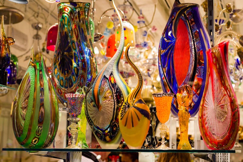 Brightly colored, and illuminated Murano glassware, decorates the front window of a Venetian store front. Items include vases, glasses, and glass sculpture. Brightly colored, and illuminated Murano glassware, decorates the front window of a Venetian store front. Items include vases, glasses, and glass sculpture.