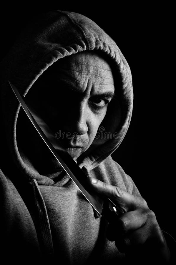 Low key image showing the concept of a violent knife wielding gang member. Low key image showing the concept of a violent knife wielding gang member