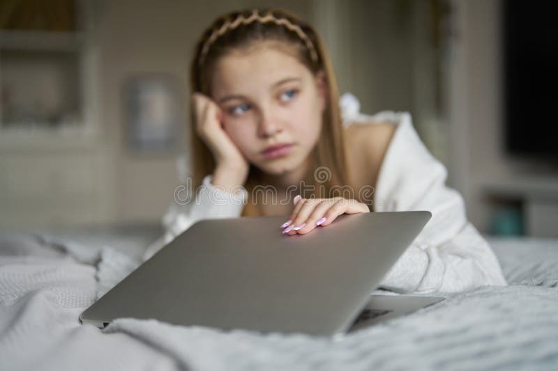 Unhappy Teenage Girl Closing Laptop Lying On Bed At Home Anxious About Social Media Online Bullying And Being Online Too Much. Unhappy Teenage Girl Closing Laptop Lying On Bed At Home Anxious About Social Media Online Bullying And Being Online Too Much