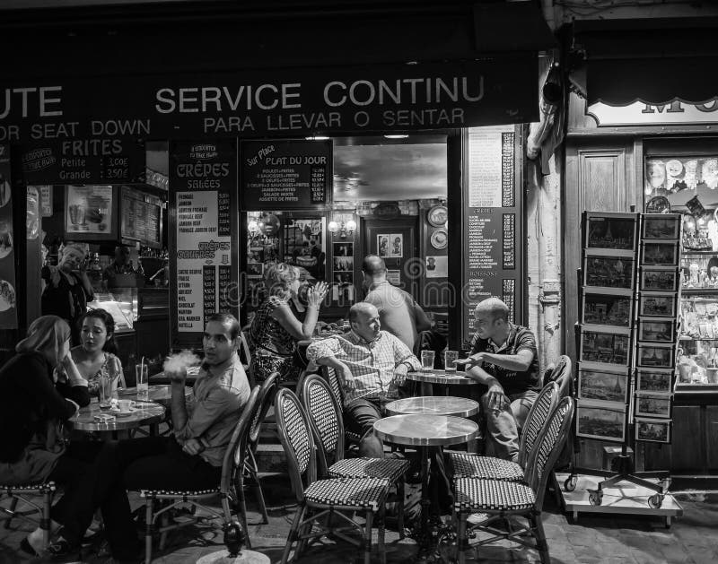 Black and white photo of drinkers in conversation at a cafe on Montmartre in Paris in the evening. Tourist postcards stand at the right side of the photo. Black and white photo of drinkers in conversation at a cafe on Montmartre in Paris in the evening. Tourist postcards stand at the right side of the photo.