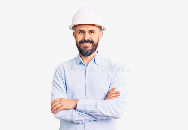 一个年轻帅气的男人，他戴着建筑师的硬帽，面带欢快的脸，双臂交叉地微笑着看着镜头 库存照片