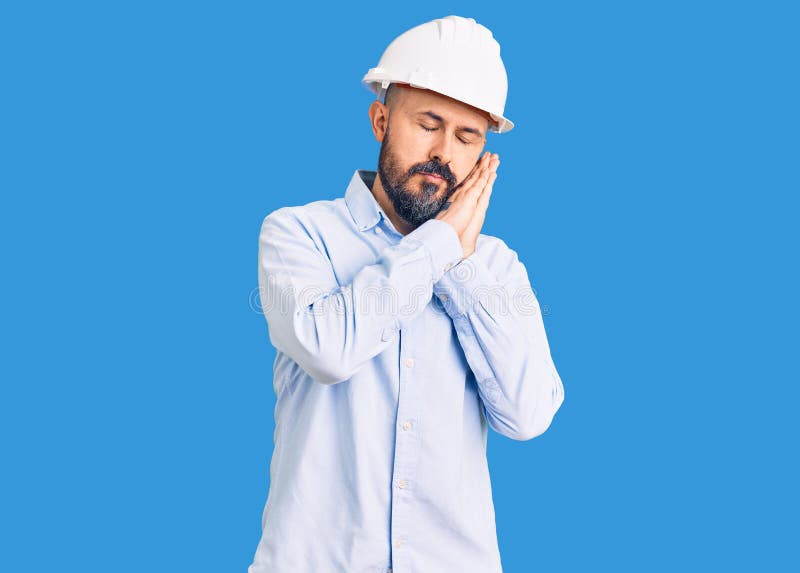 一个戴着建筑师硬帽的年轻帅哥，睡着疲惫的梦想，双手一起摆姿势，同时微笑着闭着眼睛 库存图片