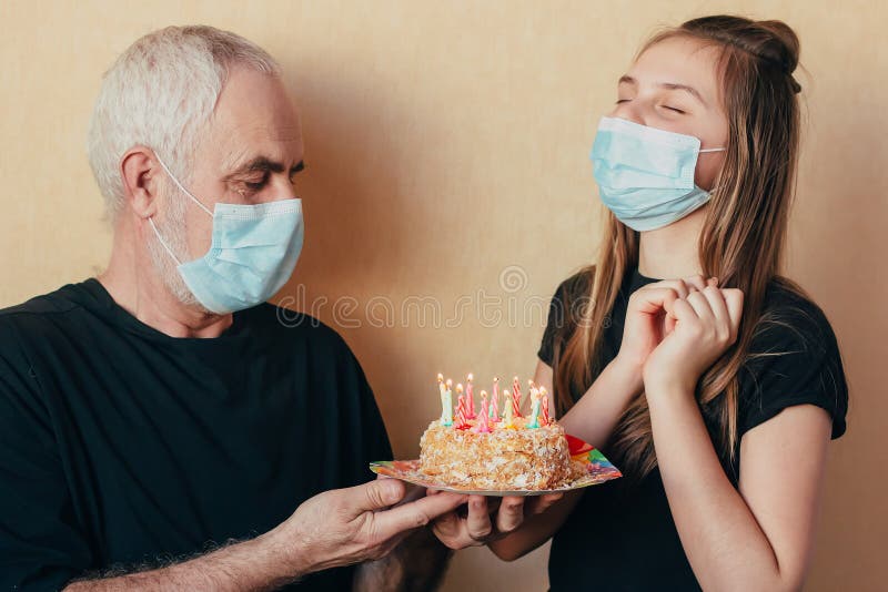 一个戴着面罩的少女许愿,老祖父给她生日蛋糕 因隔离而被破坏的假期 免版税图库摄影 一个戴着面罩的少女许愿,老祖父给她生日蛋糕 因隔离而被破坏的假期 免版税图库摄影