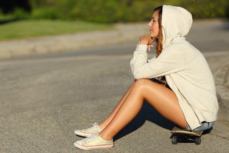 一个沉思少年女孩的档案坐在街道的一只冰鞋 库存图片