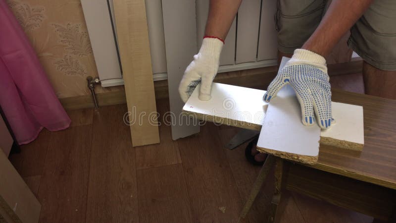 一个男人正用钢锯锯木板. 在家做家具
