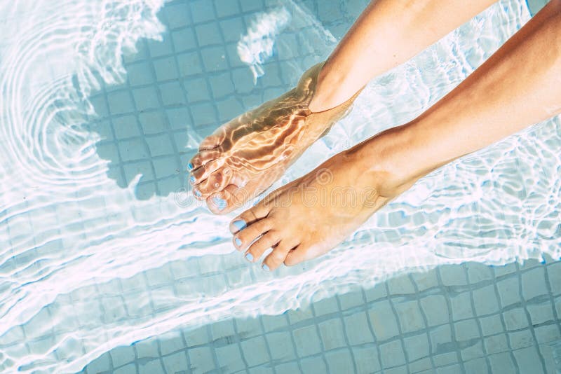 Close up of woman caucasian feet in a blue pool water and with blue painted nails - concept of trendy and beauty care in summer. Close up of woman caucasian feet in a blue pool water and with blue painted nails - concept of trendy and beauty care in summer