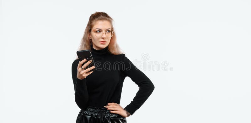 一个迷茫的年轻美女，穿着休闲服，一边看一边拿着智能手机 免版税库存图片