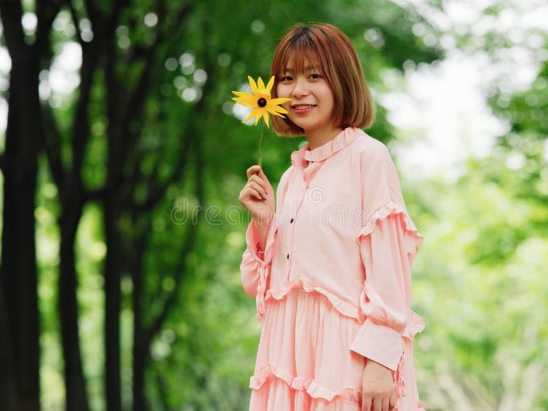 一个逗人喜爱的中国女孩的画象拿着野花和微笑对在夏天森林室外时尚画象的照相机的桃红色礼服的 免版税库存照片 一个逗人喜爱的中国女孩的画象拿着野花和微笑对在夏天森林室外时尚画象的照相机的桃红色礼服的 免版税库存照片