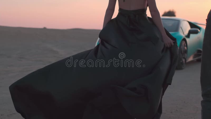 一个金发飘逸的年轻女子，穿着黑色长裙，赤脚在沙漠沙地上走到一处昂贵的地方