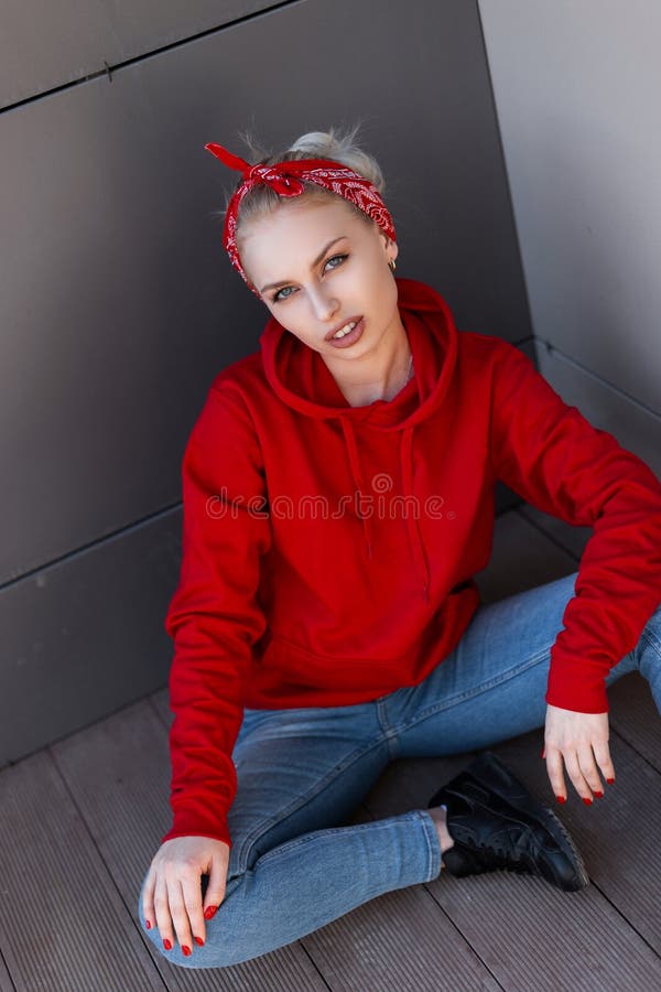 一件时髦红色戴头巾运动衫的美国现代年轻白肤金发的妇女在皮靴的一块红色班丹纳花绸在蓝色牛仔裤 库存照片 一件时髦红色戴头巾运动衫的美国现代年轻白肤金发的妇女在皮靴的一块红色班丹纳花绸在蓝色牛仔裤 库存照片