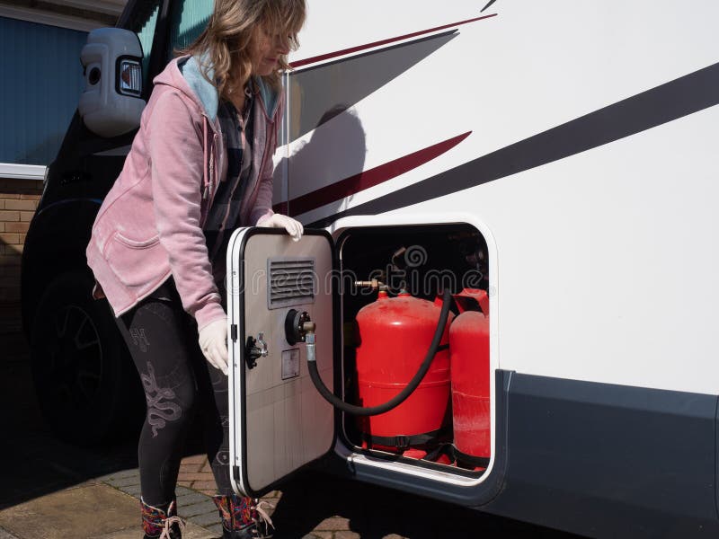 A lady motorhome owner opens a gas locker door of her recreational vehicle wearing gloves.Red LPG gas bottles can be seen. A lady motorhome owner opens a gas locker door of her recreational vehicle wearing gloves.Red LPG gas bottles can be seen.